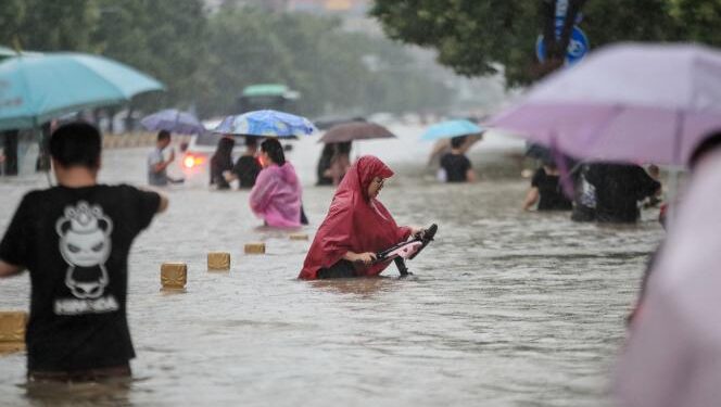 Inondations en Chine : L'Egypte présente ses condoléances 1 - Le Progrès Egyptien TOPSHOT - This photo taken on July 20, 2021 shows people wading through flood waters along a street following heavy rains in Zhengzhou in China's central Henan province. - China OUT (Photo by AFP)