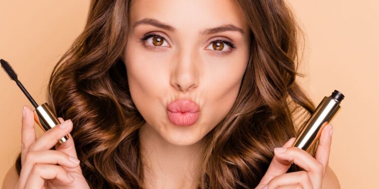 Close up photo of charming, pretty girl hold mascara prepare for date look at mirror send air kisses isolated over pastel color background