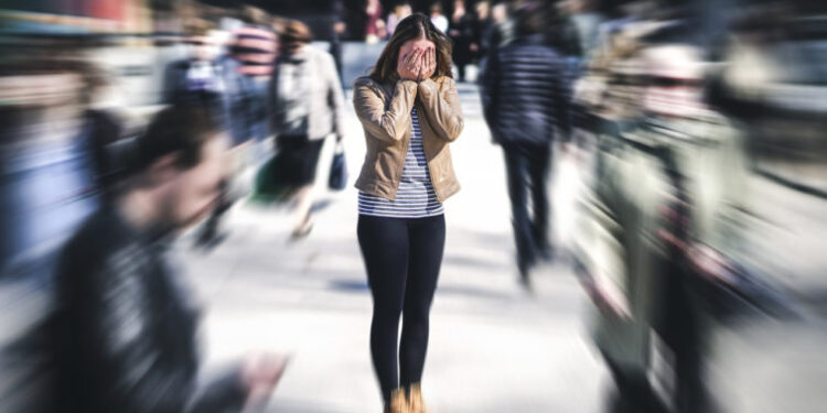 Panic attack in public place. Woman having panic disorder in city. Psychology, solitude, fear or mental health problems concept. Depressed sad person surrounded by people walking in busy street.