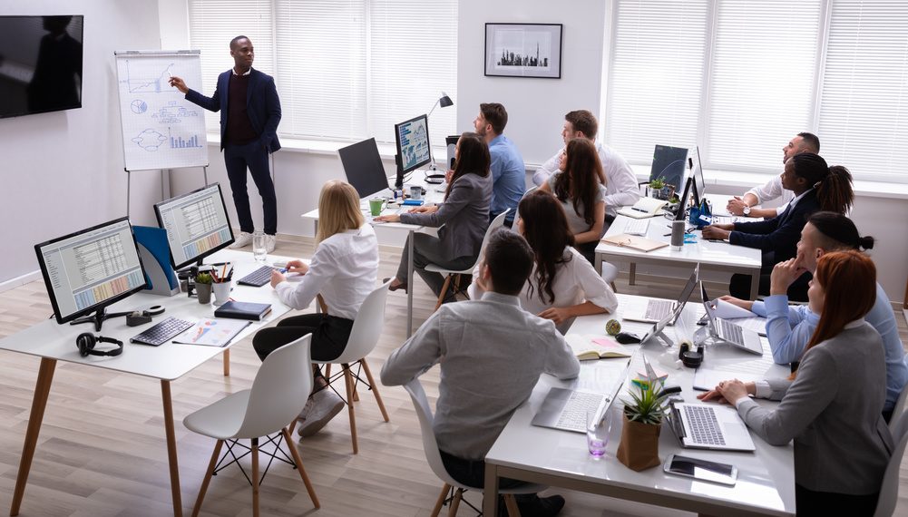 Egypte-Pays-Bas: Examen de la coopération dans la formation professionnelle 1 - Le Progrès Egyptien African Businessman Giving Presentation To His Colleagues Sitting On Table With Computers In Office