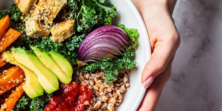 Baked vegetables, avocado, tofu and buckwheat buddha bowl. Vegan lunch salad with kale, baked sweet potato, tofu, buckwheat and avocado in a white bowl. Vegan concept.