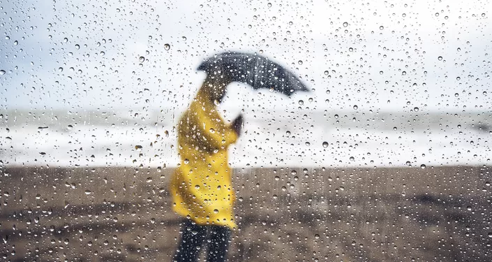 Man walking on the beach under heavy rain, viewed through windshield with raindrops