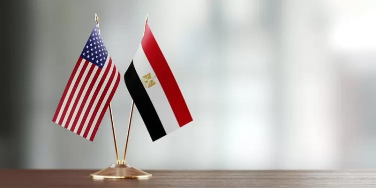 American and Egyptian flag pair on desk over defocused background. Horizontal composition with copy space and selective focus.